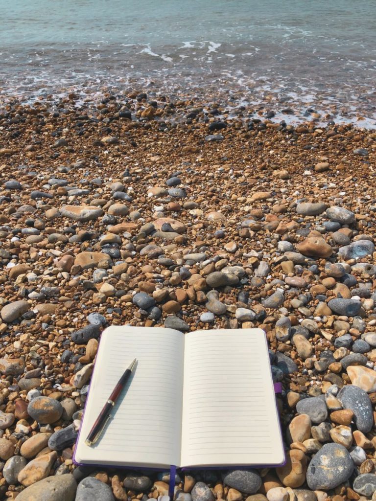 An blank notebook and pen on a pebble beach by the sea